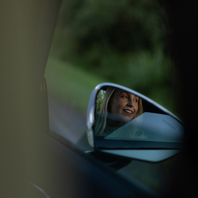 Nuori ihminen katsoo auton ikkunasta ja hymyilee.